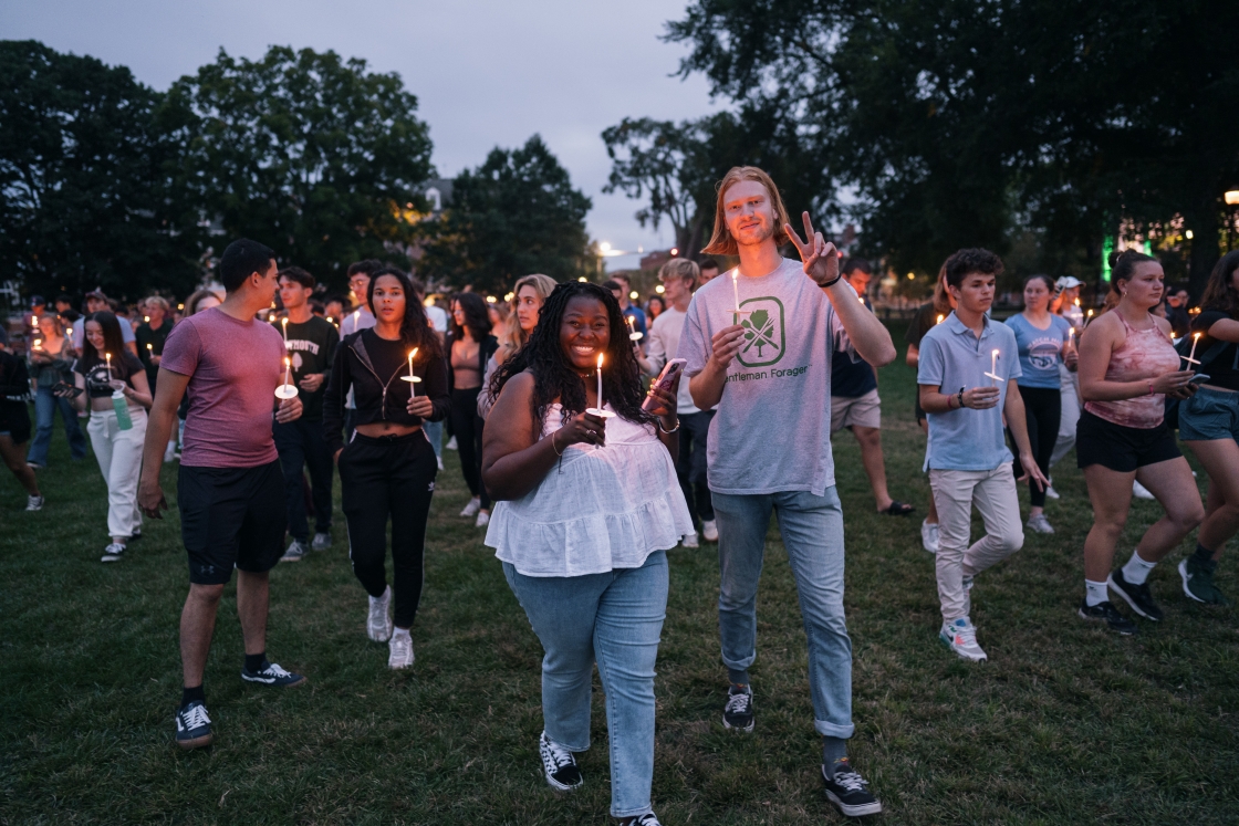 Students walk across campus at dusk holding candles