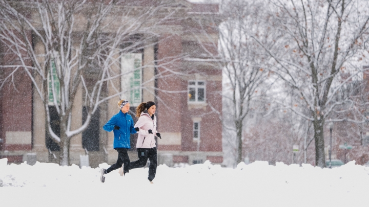 Two students running in the snow in front of Rauner Library