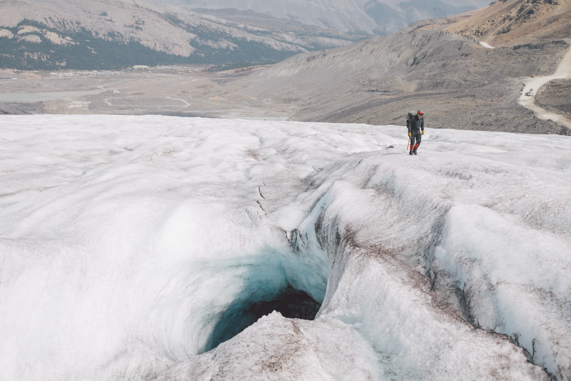 On the Athabasca Glacier, Associate Professor Robert Hawley walks by a moulin, where meltwater has drilled through the glacier surface.