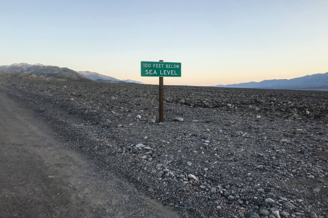 A green sign reads 100 feet below sea level in Death Valley, Calif.