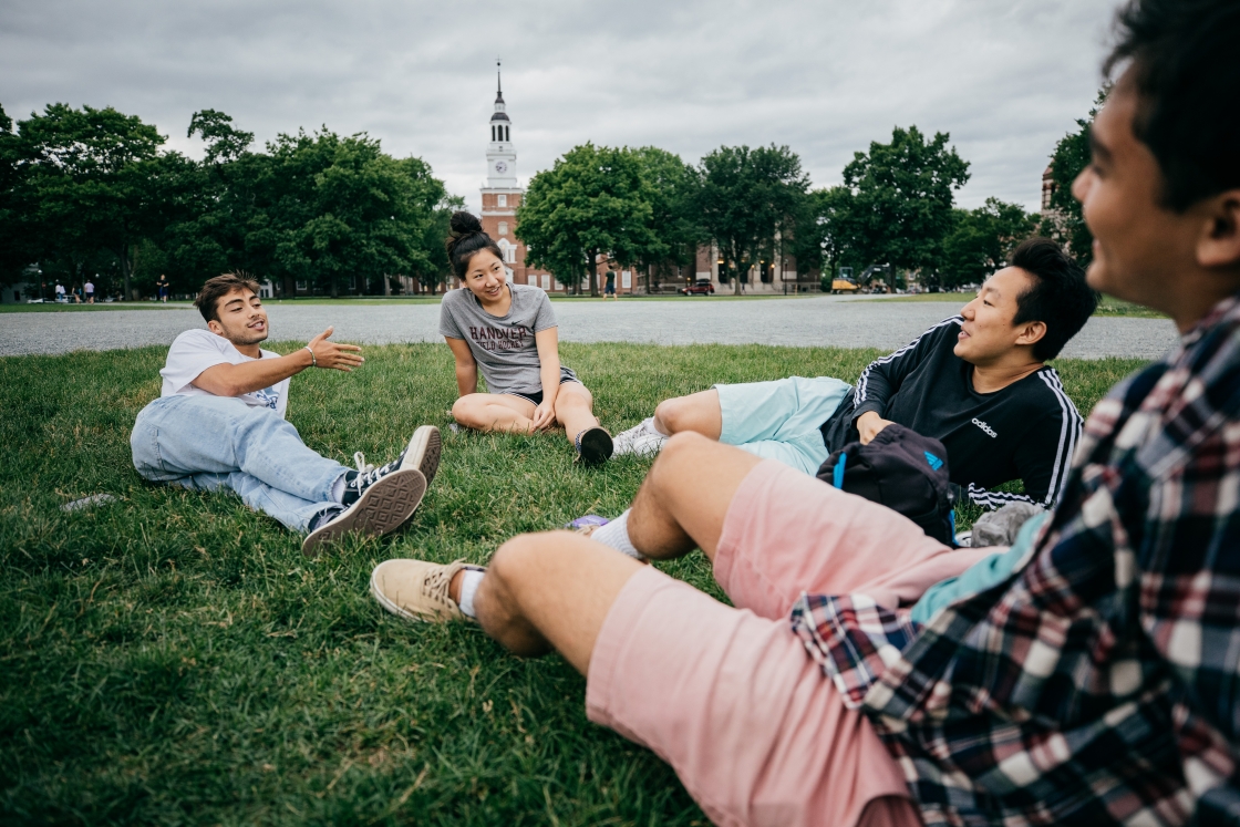 Four students sitting on campus green, talking