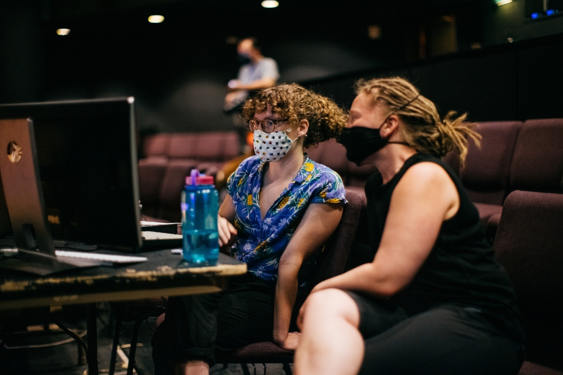 Two masked people in front of a monitor