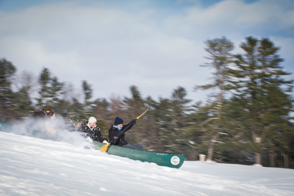 Students racing down a ski slope in a green canoe