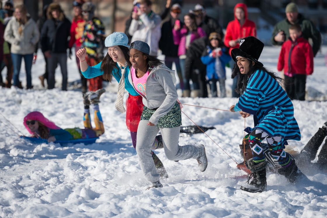 Three women racing across the snow, pulling a sled, and wearing swag