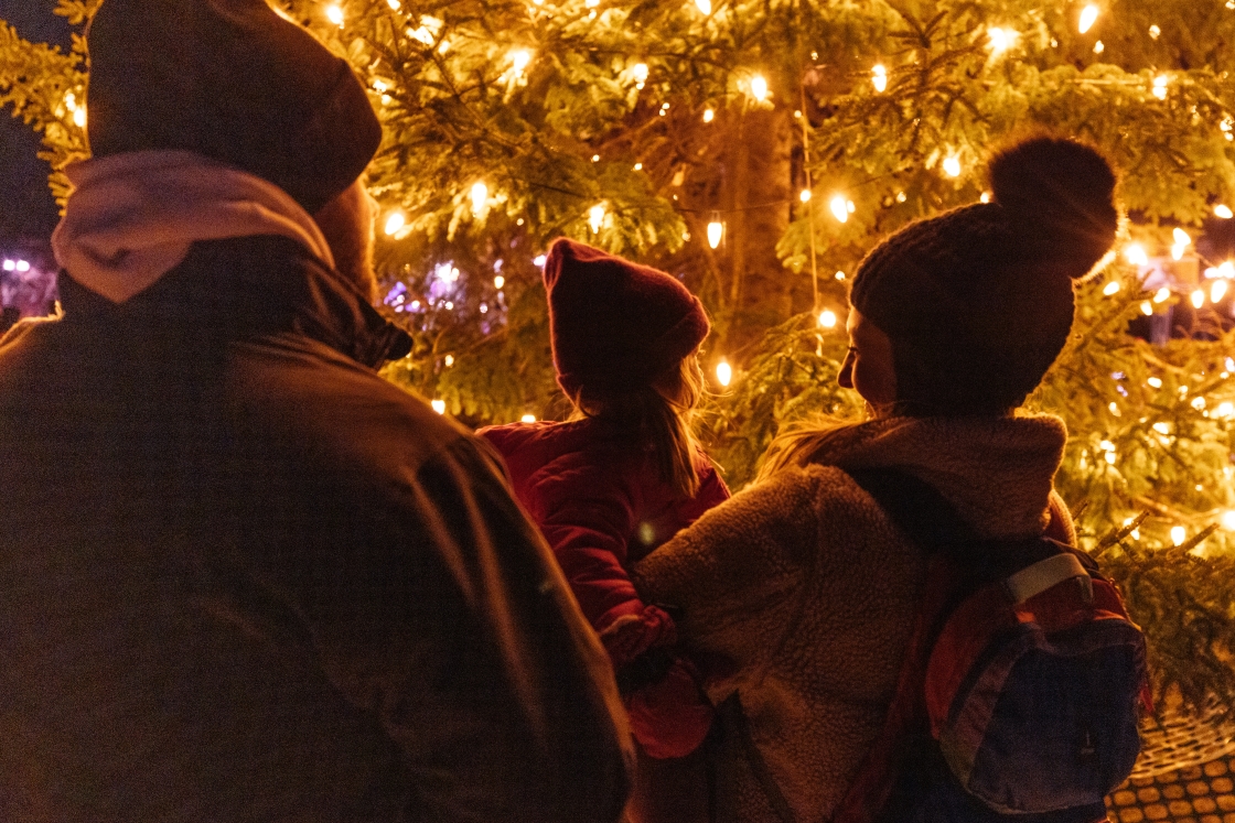 Family of three looking at lit Christmas tree upclose