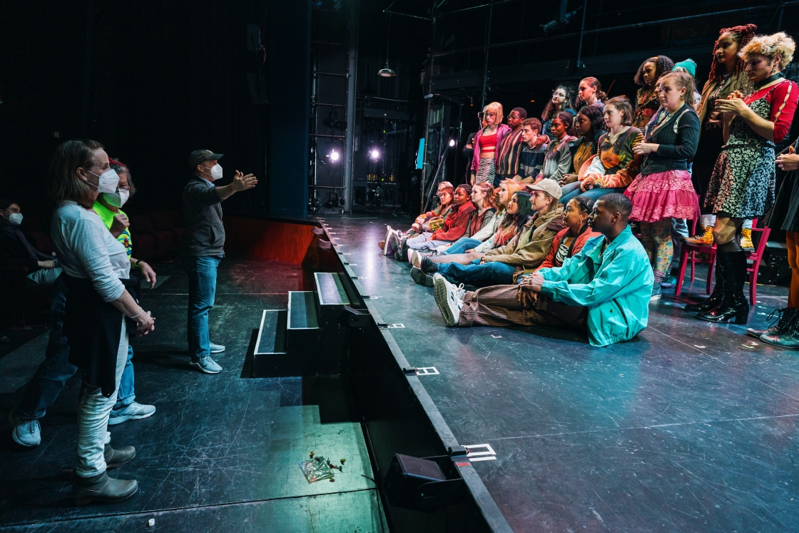 Students sit and stand on the stage in the performance of RENT