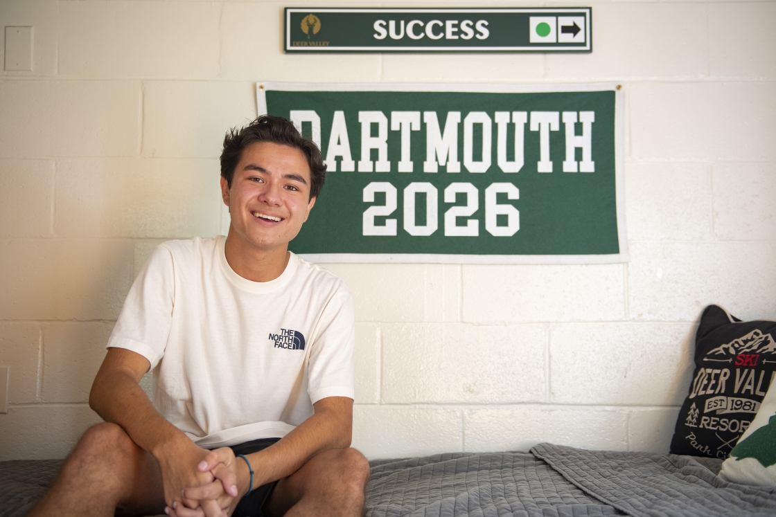 Student sits on bed in front of Dartmouth 2026 sign