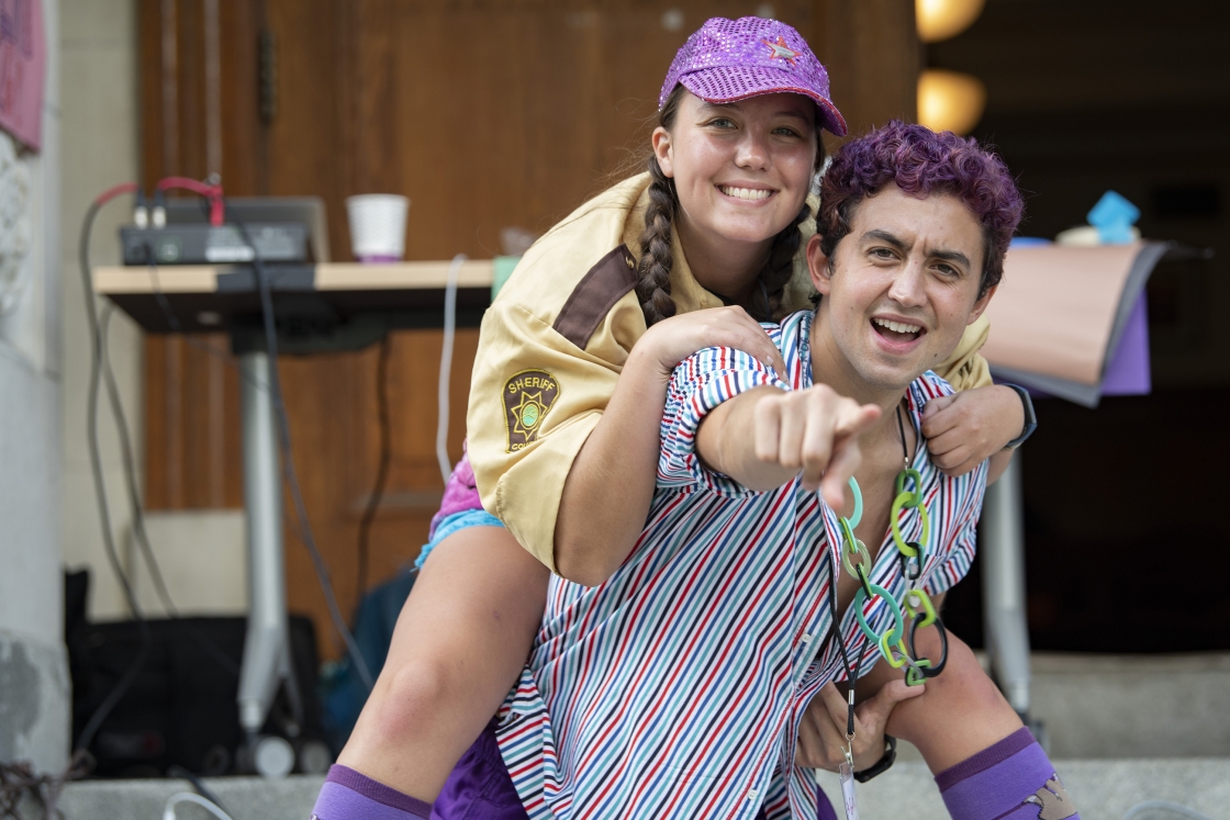 Students with purple hair and purple hat smile at the camera