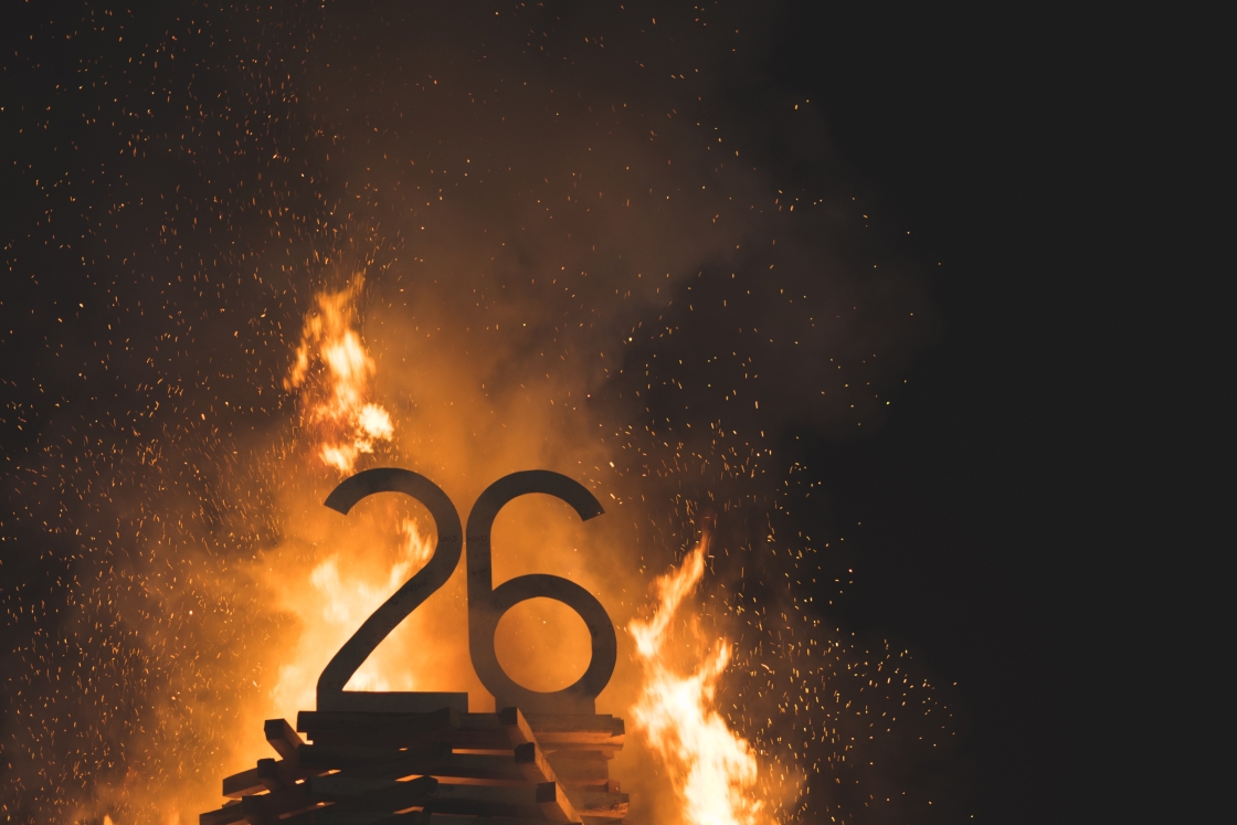 Flames reach the top of the bonfire structure and consume the &quot;26.&quot;