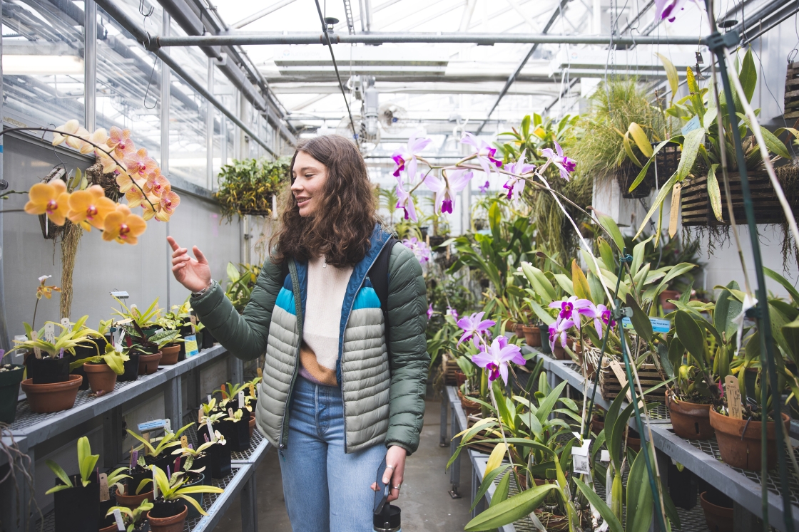 Emma Borchers pointing at an orange orchid