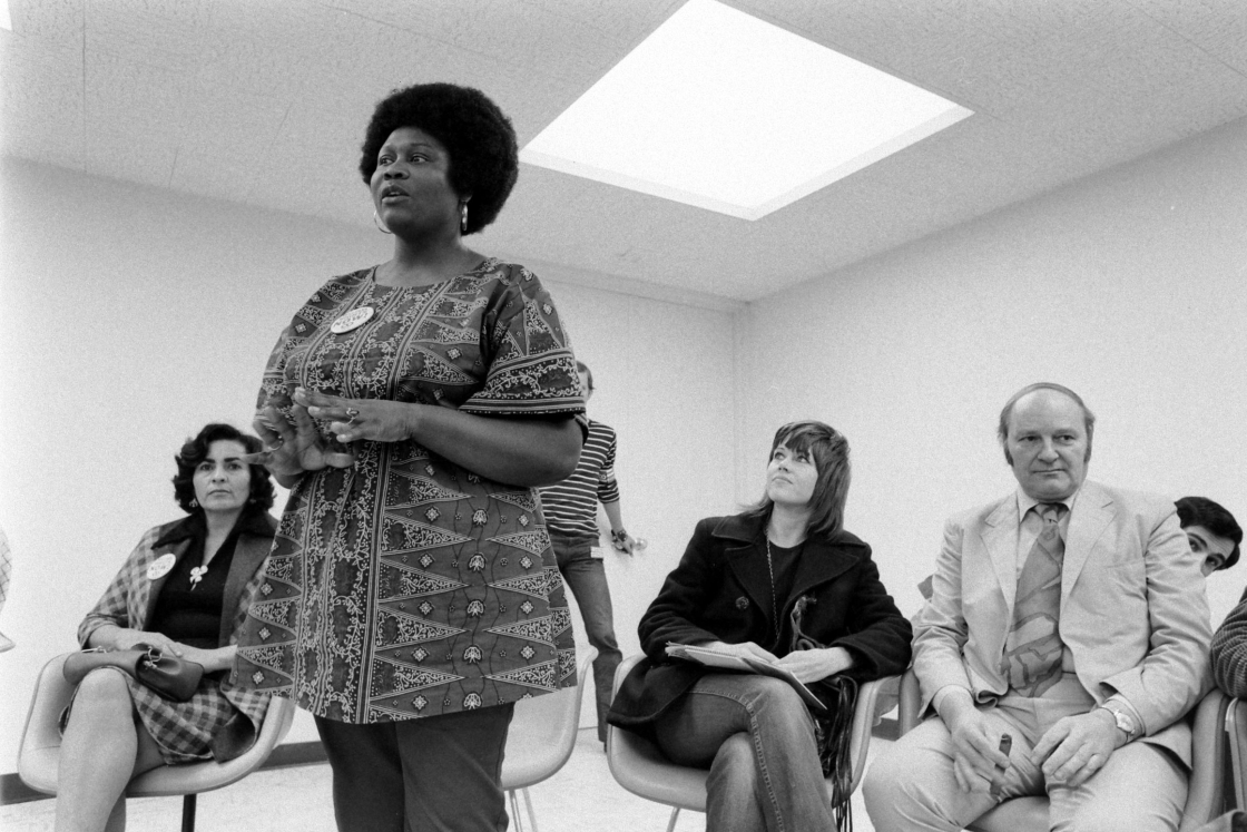 Ruby Duncan standing and addressing group, with Jane Fonda seated and listening on the eve of the Strip march in 1971.