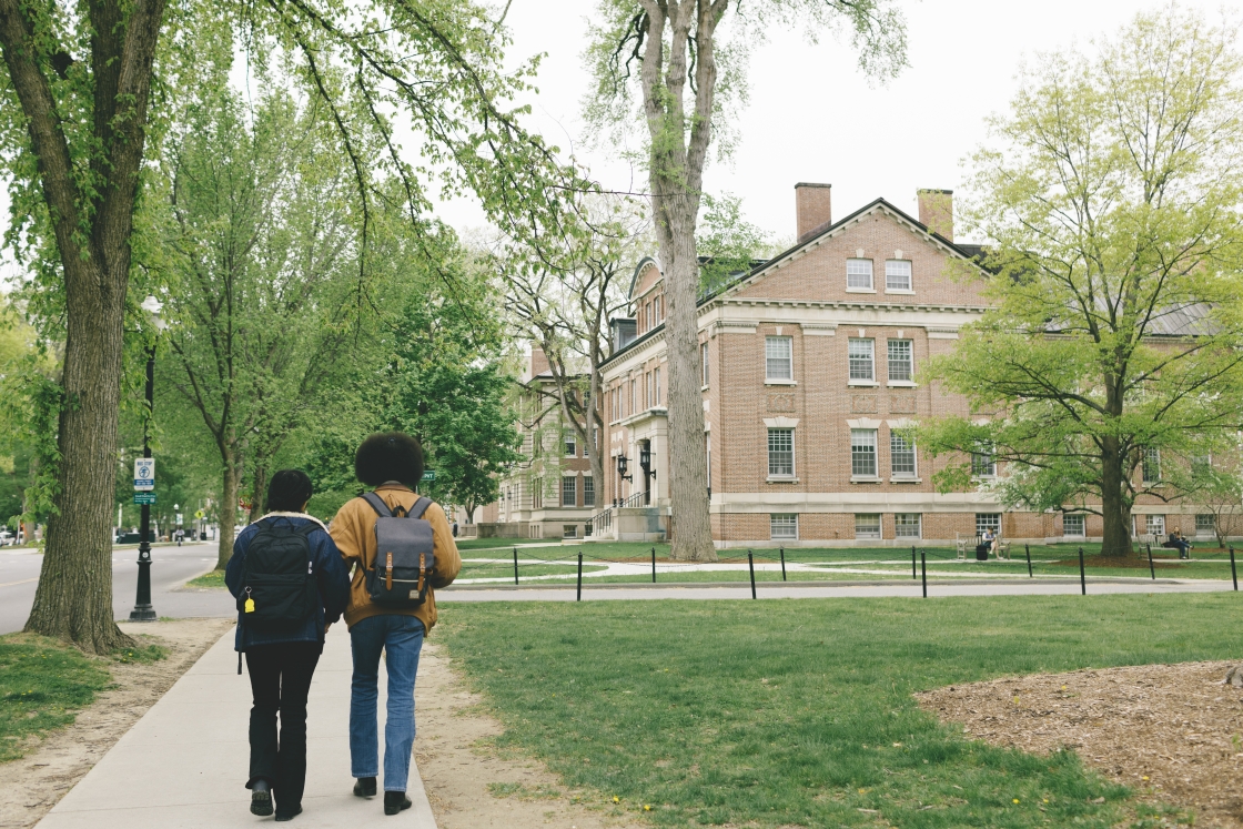 Two students walking to class as green leaves and grass return to campus
