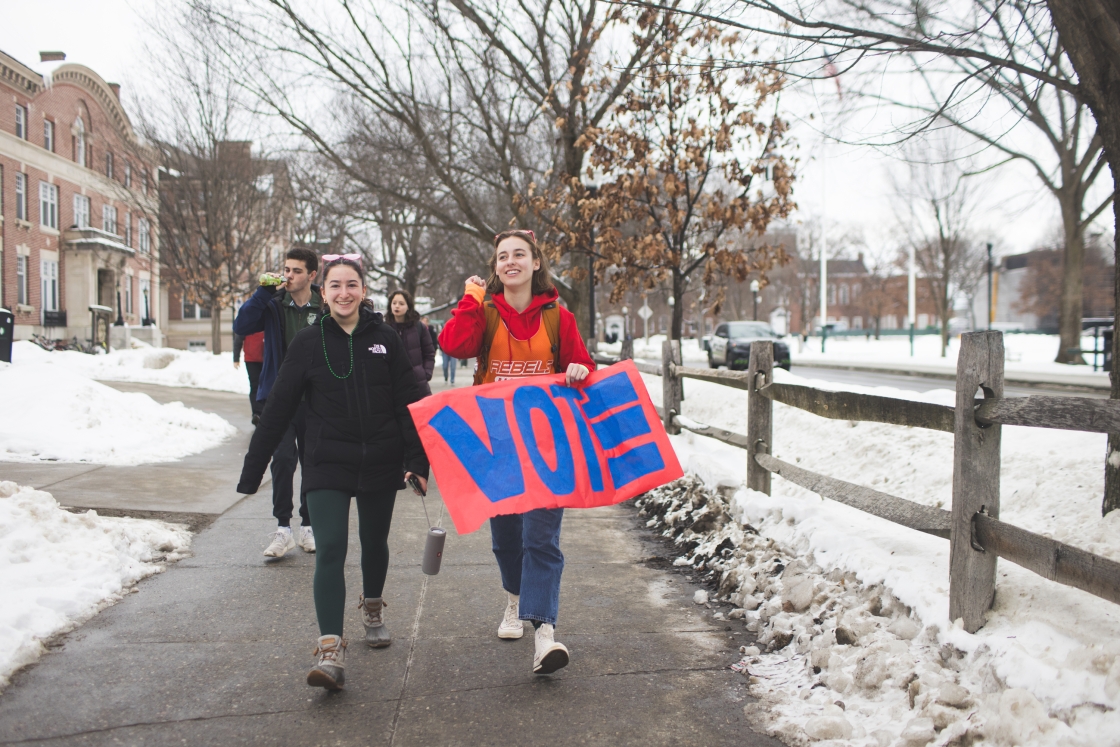 Two students holding a colorful VOTE sign lead students to vote.