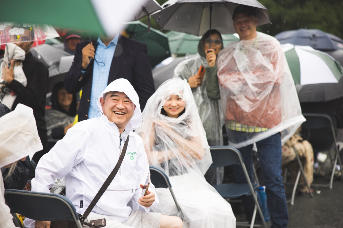 Parents at Dartmouth Commencement stand in the rain with umbrellas