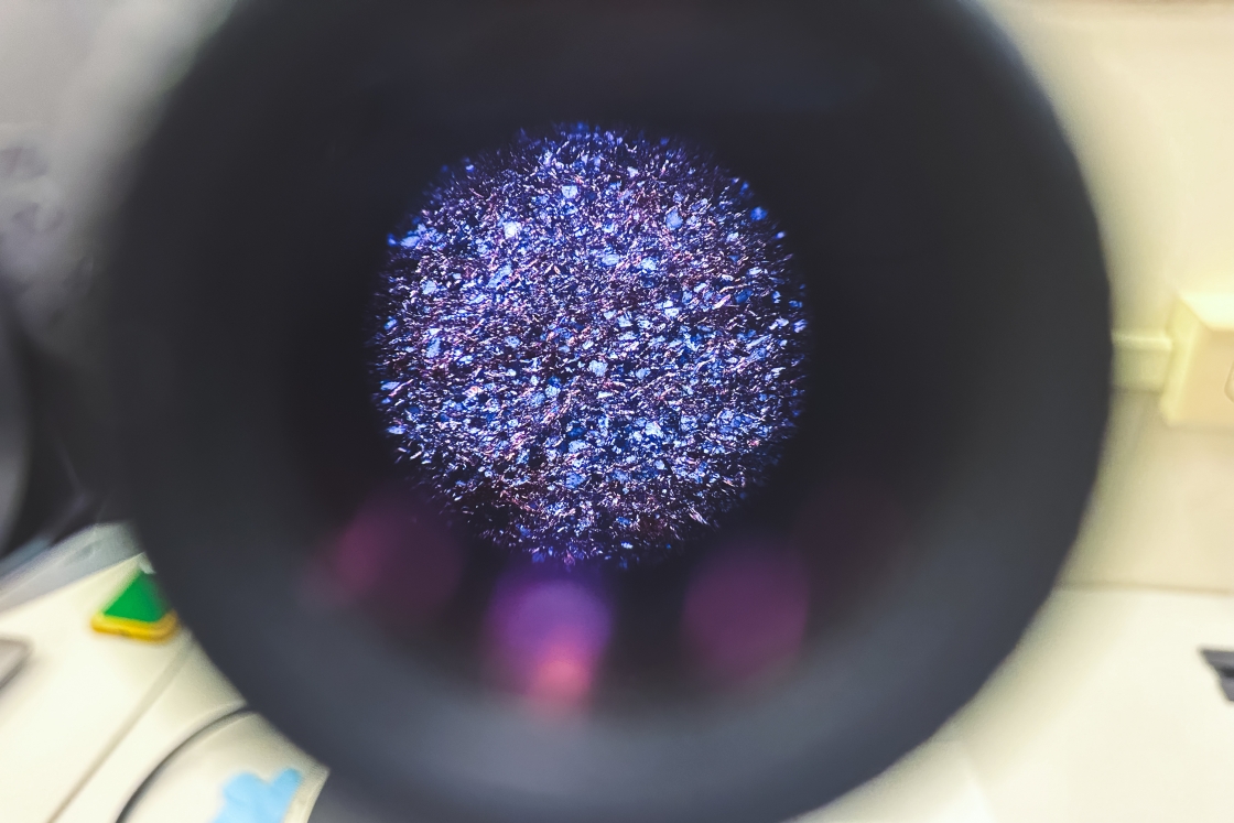 Peering down the view window of a microscope at the purplish ferruginous shale