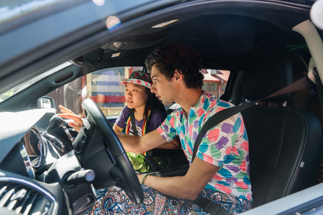 A picture of Jack Kreisler '22 in the driver seat of the Vox van and Emma Demers '20 is sitting in the front passenger seat. Both are wearing colorful attire.