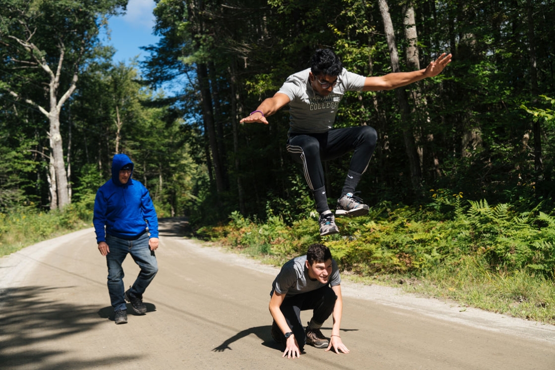 Gokul Srinivasan '23 jumps over Blake Danziger '23 who is crouched down. They are on a dirt road and Evan Antich '23 is walking behind them.
