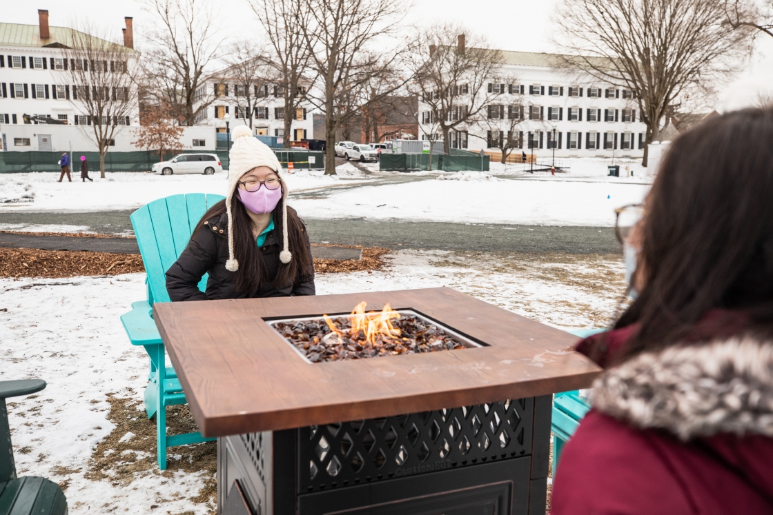 Two students sit by a fire pit.
