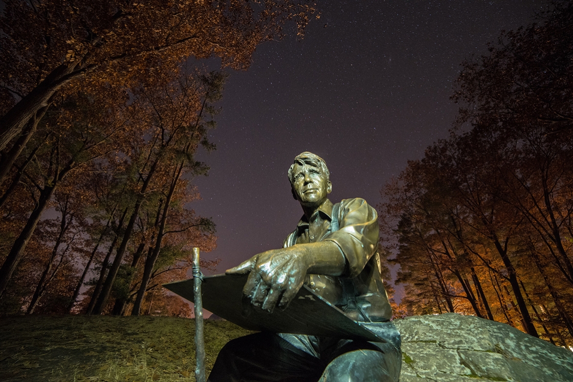 The statue of Robert Frost looks out over a clear fall night.