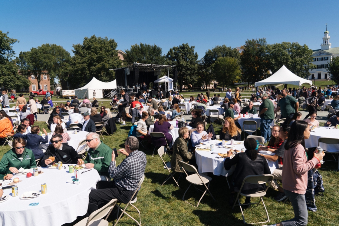 Several tables are set up on the Dartmouth Green with people enjoying a cookout while listening to music performers on a stage at the north end of the green.