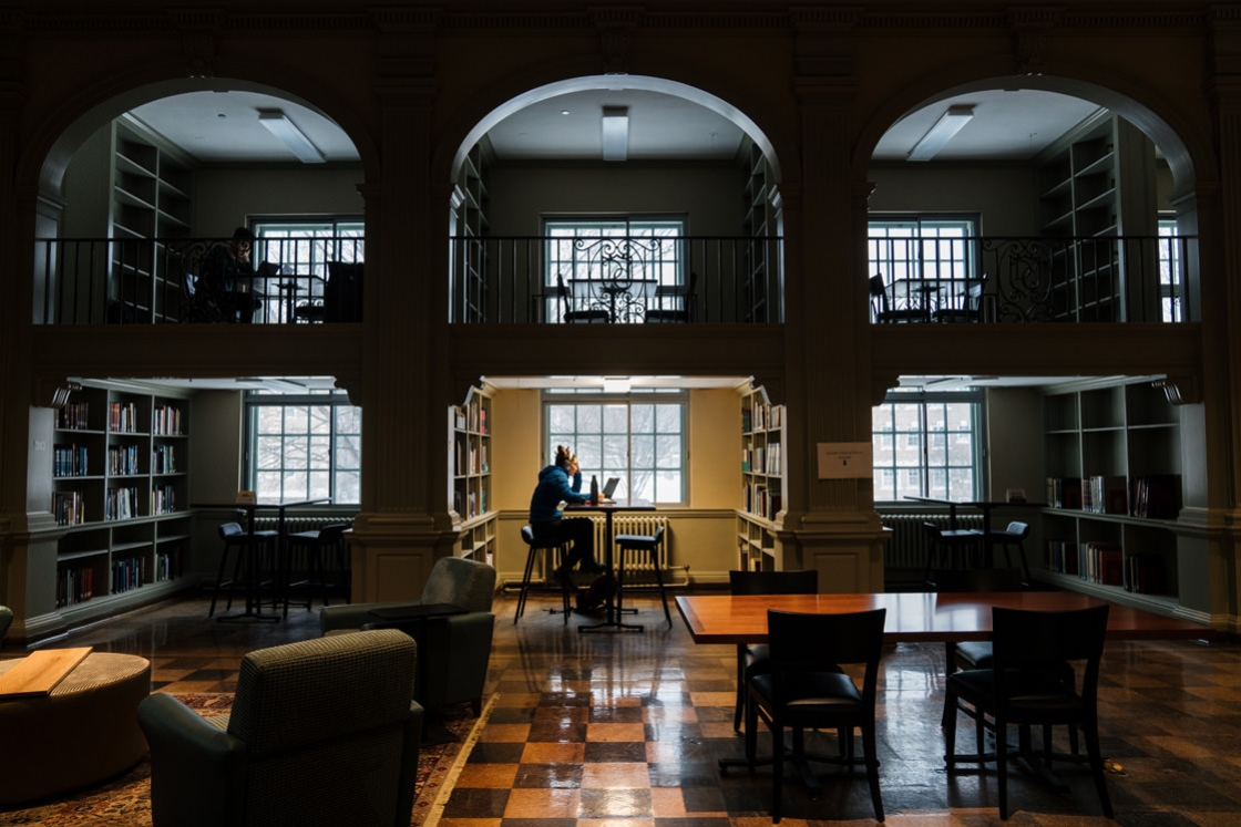 Student sits alone reading in Baker-Berry Library's Treasure Room. It is dark and there is a single light above her.