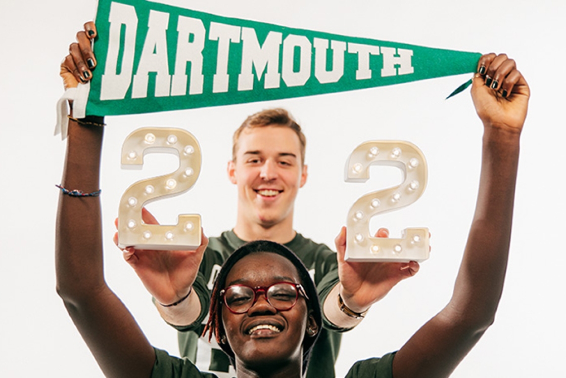 a female student holding a Dartmouth pennant above her head and a male student holding the number 22 behind her