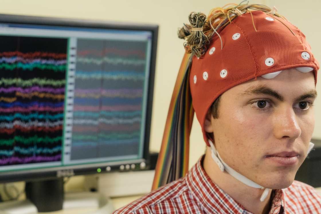 a research assistant wearing a red cap with wires connected to it