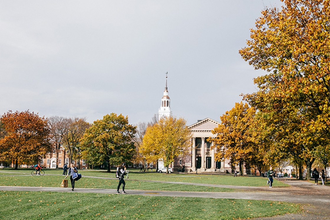 students walking across the Green with yellow foliage and Baker Tower in the background