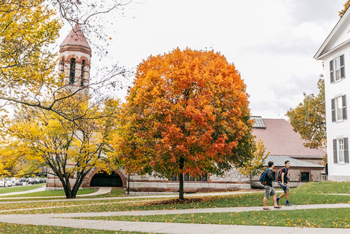 Two students walk to Dartmouth Hall in the fall with Rooke Chapel in the background