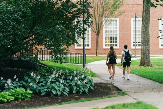 Two students walking past a garden of hostas toward Baker Library after a summer rain storm..