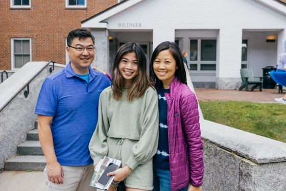 Three person family poses in front of dorm