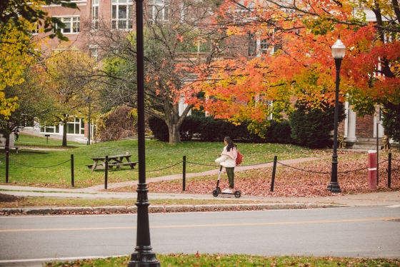 Student riding an escooter through the fall leaves