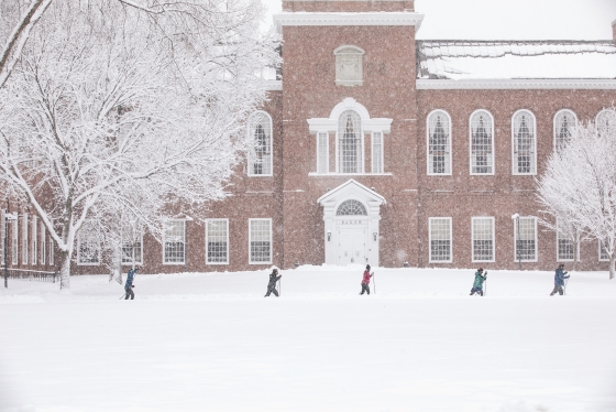Five people nordic skiing in front of Baker-Berry library in a snowstorm