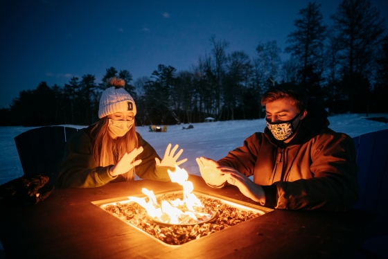 Two people warming their hands around a firepit