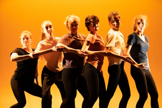 Members of dance troupe Dartmouth Dance Ensemble performing against an orange background