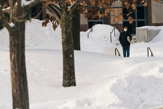 Student near snowdrifts holding coffee cup