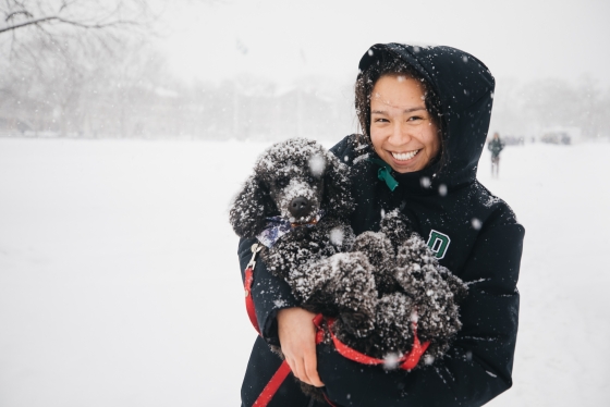 Student holding black poodle covered in fresh snow
