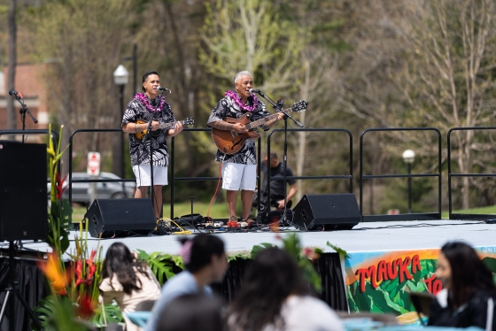 Two men in leis singing onstage with guitar and ukulele