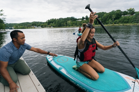 Student pushing off the dock in paddle board with assistance from staff