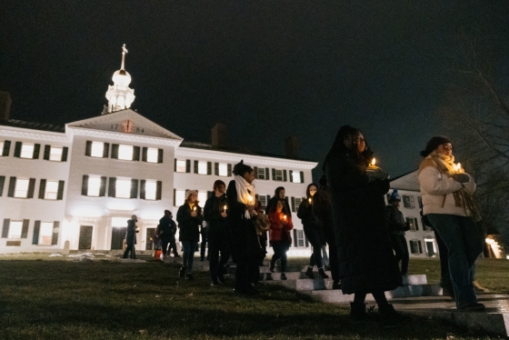 Students hold candles and walk out of Dartmouth Hall at night
