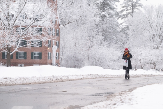 A woman scooters down a road on campus in the snow