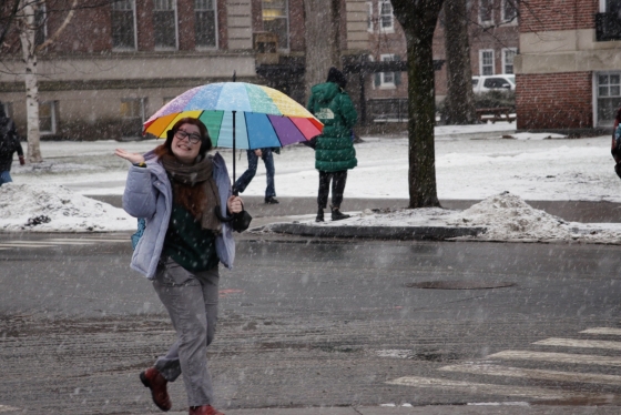 A student waves under a rainbow umbrella during snowfall