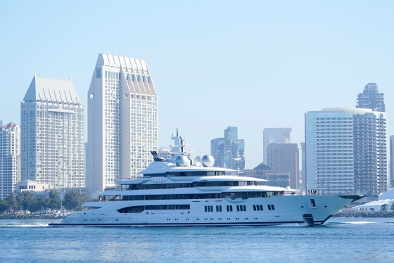 Large yacht traveling on water with city in the background.