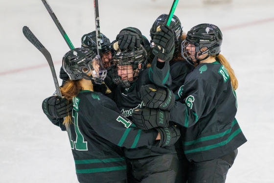 Women's hockey team embracing on the ice after a goal