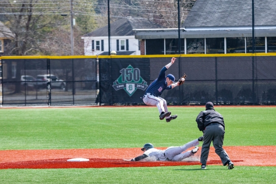 A baseball player leaps in the air to avoid a runner sliding under him at second base.