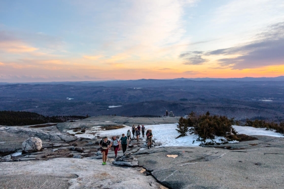 Students hike up Mount Cardigan as the sun sets behind them.