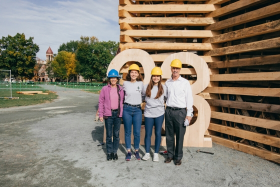 President Phil Hanlon '77, far right, and his wife, Gail Gentes, far left, pose with bonfire build committee co-chairs Antonina Zakorchemna '23, center left, and Katie Glance '23, center right, at the structure's base.