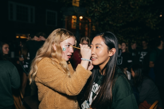 A female students applies face paint to another female student outside on Dartmouth Night.
