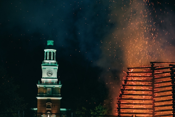 Embers from Dartmouth Night's bonfire sail to the sky against the backdrop of the greenlit Bakery Library Tower.