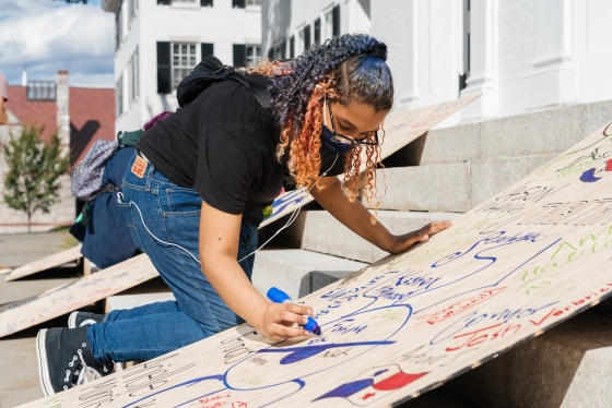 A masked student signs one of the plywood homecoming boards to be burned at the 2021 homecoming bonfire.